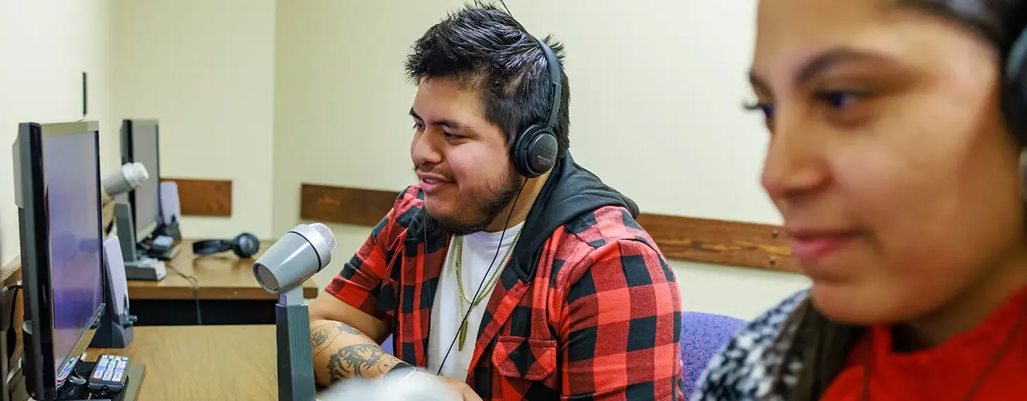 Two students wearing headphones observing a social work exercise with microphones and computers.